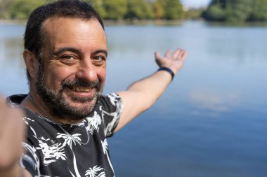 Aktif yakışıklı, olgun, beyaz bir adam gölde selfie çekiyor. Açık hava macera konsepti.