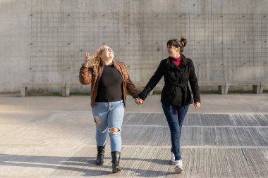 Latin lezbiyen çift sokakta el ele yürürken birbirlerine sevgiyle bakıyorlar.