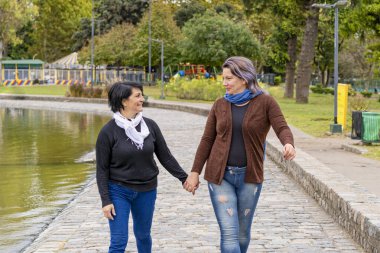 Parkta el ele tutuşup birbirlerine bakan lezbiyen çift.