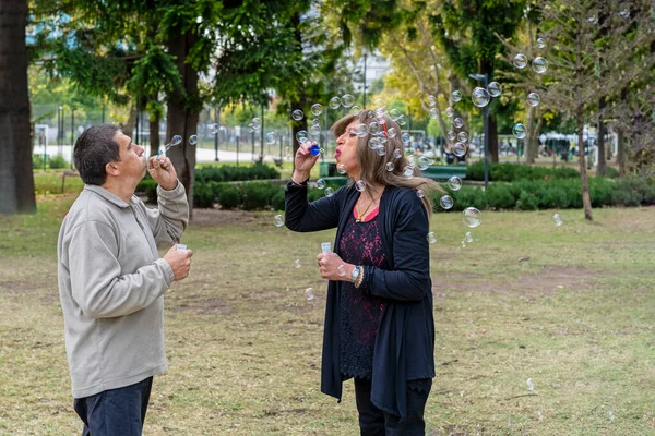 Cheerful mature queer couple blowing bubbles in a park