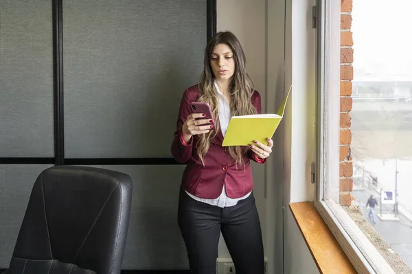 Young blonde business woman in her office using the phone while checking notes
