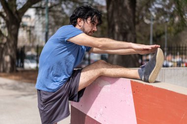 Yakışıklı, olgun sakallı, atletik bir adamın portresi. 40 'lı yaşlarda, esneme egzersizi yapıyor. Parkta sabah antrenmanına hazırlanıyor.