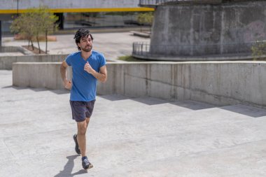 Yakışıklı, olgun sakallı, atletik adamın portresi. 40 yaşlarında, mavi tişörtlü, merdivenlerde koşuyor..