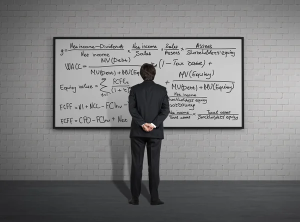 Businessman standing in front of board with formulas — Stock Photo, Image
