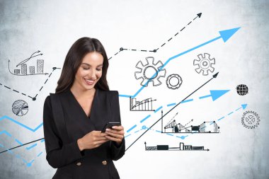 Takım elbiseli çekici güler yüzlü iş kadını, yeni fikirlerle başlamak için bir araştırma yapmak amacıyla akıllı telefonuyla internete göz atıyor. İş akış çizelgeleri ve grafikleri beton duvara çizildi.