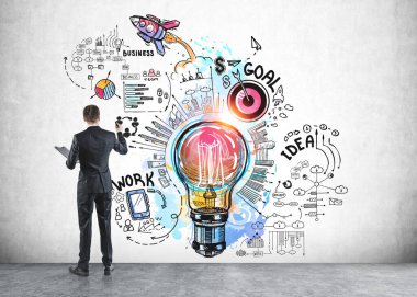 Resmi takım elbiseli iş adamı notlar alır ve elinde ampul, roket fırlatma, çark, iş, plan, duvarda takım çalışması olan bir robot resmin yanında durur. Hayal gücü kavramı ve yaratıcı fikirler için ilham.