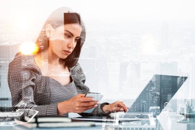 Ofisteki kadın telefonu kullanıyor, dizüstü bilgisayara ciddi ciddi bakıyor. New York 'taki binalarla çifte temas. İş sekreteri ve teknoloji kavramı