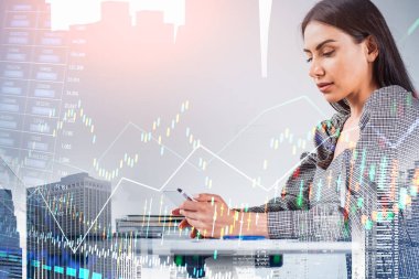 Gri elbiseli iş kadını akıllı telefondan mesaj yazıyor. New York şehrinin gökdeleni, finansal grafiği ve grafiği. Arka planında da Forx Candlestick var. Başarılı ticaret kavramı