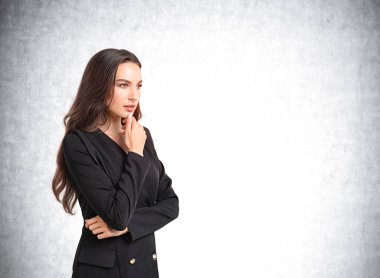 Resmi takım elbiseli genç çekici iş kadını çapraz kol pozisyonunda duruyor. Arka planda boş beton duvar var. Başarılı kariyer, liderlik, kalkınma ve ticaret kavramı