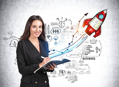 Siyah ceketli çekici bir kadın not defterine not alıyor ve başarılı olmanın hayalini kuruyor. Başarı kavramı ve yeni iş projeleri. Beton duvara roket çizimi