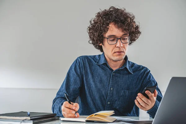 Curly Serious Businessman Wearing Jeans Shirt Taking Notes Holding Smartphone — Stock Photo, Image