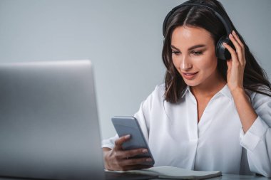 Kadın telefon ekranına bakıyor, odaklanmış görüntü ve podcast dinliyor, müzik dinliyor. İşletme öğrencisi, bilgisayarla uzaktan eğitim. E-öğrenme kavramı