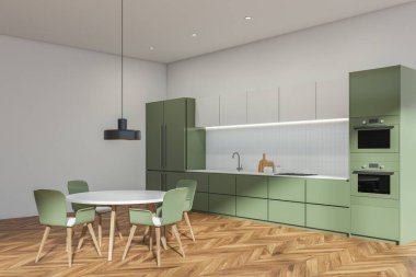 Yuvarlak masalı açık mutfak seti ve parke üzerinde lamba olan yeşil sandalyeler. Modern mobilyalar, yan görüş, güvertede mutfak gereçleri ve buzdolabı fırınıyla minimalist iç mekan.