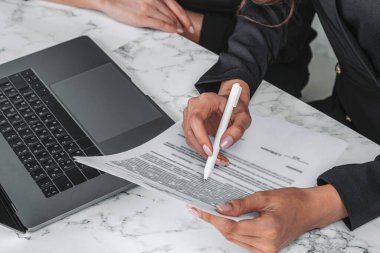 Kontratta kalem ucu olan ofis çalışanı, yakın plan. İki kişi dizüstü bilgisayar ve iş belgeleriyle birlikte çalışıyor. Takım çalışması ve mali anlaşma kavramı