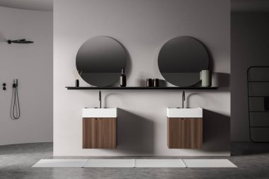 White bathing interior with two sinks and round mirrors with accessories on rack, grey concrete floor and foot towel, douche and rail ladder on background, 3D rendering