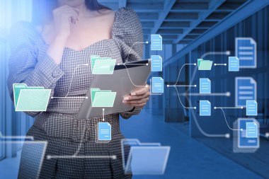 Tabletle çalışan iş kadını, arka planda ofis odasına dalgın dalgın bakıyor. Belge simgelerinin olduğu klasörler. İş bilgileri için bulut depolama, çevrimiçi veritabanı. Yönetim kavramı