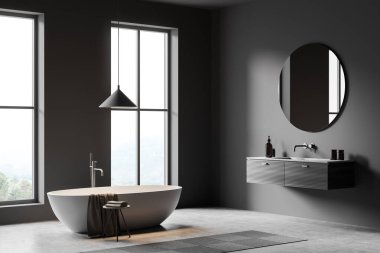 Gri küvetli gri çamaşır odası, yuvarlak aynalı lavabo, gri beton zeminde ayak havlusu. Güvertede banyo aksesuarları, yan görüş, kırsal alanda panoramik pencere. 3B görüntüleme