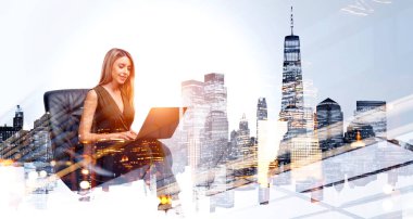 İş kadını ofis koltuğunda oturuyor, dizüstü bilgisayarla çalışıyor, gülümsüyor. New York şehir manzarasında panoramik manzara, tonlu görüntü. Finans ve teknoloji kavramı
