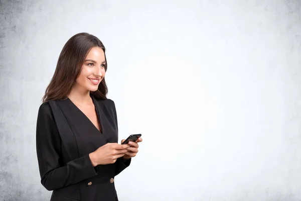 Uśmiechnięta Młoda Atrakcyjna Bizneswoman Garniturze Trzyma Smartfona Pusta Betonowa Ściana — Zdjęcie stockowe