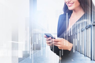 Resmi takım elbiseli gülümseyen iş kadını elinde akıllı telefon tutuyor. Arka planda panoramik pencereler olan ofis işyeri. Hayal gücü kavramı ve yaratıcı fikirler için ilham.