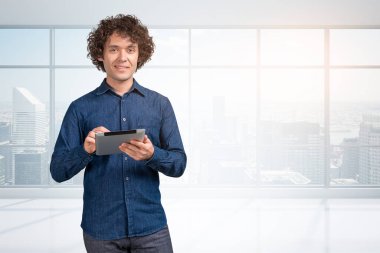 Üzerinde kot gömleği olan bir iş adamı, kameraya mutlu bir şekilde bakın. New York manzaralı panoramik pencere. Programlama ve iş teknolojisi kavramı