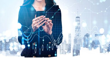 Resmi takım elbiseli bir iş kadını akıllı telefondan mesaj yazıyor. Arka planda New York gökdelenleri var. Eski şamdan, mali grafik ve çizelge ön planda. Ticaret kavramı