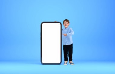 Gömlek ve spor ayakkabı giyen gülümseyen yakışıklı çocuk boş akıllı telefonlara dokunuyor. Mavi arka plan. Hayal gücü kavramı ve yaratıcı fikirler için ilham.