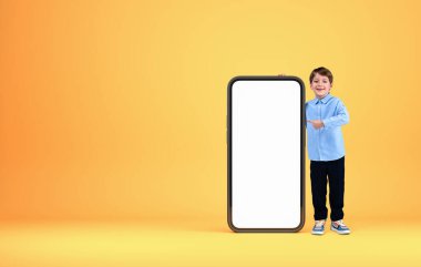 Küçük bir çocuk gülümsüyor, uzun boylu, akıllı telefonu işaret ediyor kopya uzay ekranı, sarı arka plan. Teklif ve tavsiye kavramı. 3B görüntüleme