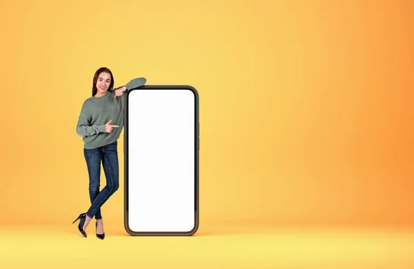 スマートフォンのモックアップコピースペース画面 黄色の背景で若い女性の笑顔 フル長さ 指ポイント 新しいウェブサイトの概念 3Dレンダリング — ストック写真