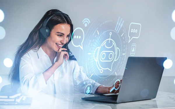 Businesswoman in headphones laugh, typing on laptop, hologram of voice chat. Hud with bot icon and social network. Office table with computer. Concept of video call and artificial intelligence