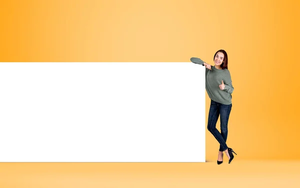 Woman gives like, thumb up, smiling near empty canvas. Mockup blank whiteboard on yellow background. Concept of feedback and recommend