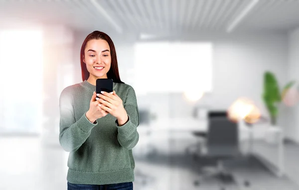 Young woman with a happy smile, using mobile app. Lady looking at smartphone, blurred background of office room. Concept of business offer and recruitment