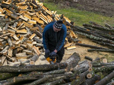 Ön planda odun, odun ve kütük kesen bir adamın resmi.