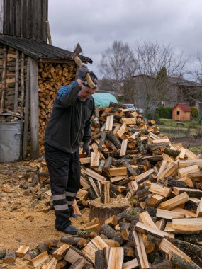 Ön planda kütüklerle odun kesen bir adamın resmi.