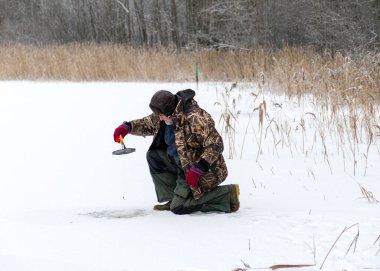 Güneşli bir günde buz nehrinin üzerindeki kış manzarası. Kış sporları, balıkçı gölde buzda balık tutmayı, gölde kış balıkçılığını sever..