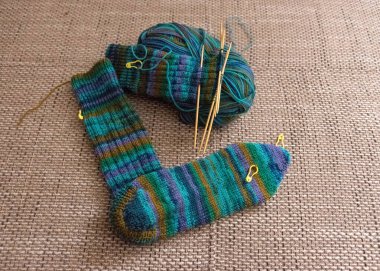 Yeşil çizgili iplikle örülmüş çorap, ahşap örgü iğneleri, yün yumağı, hobi olarak el işi, örgü konsepti, el işi.