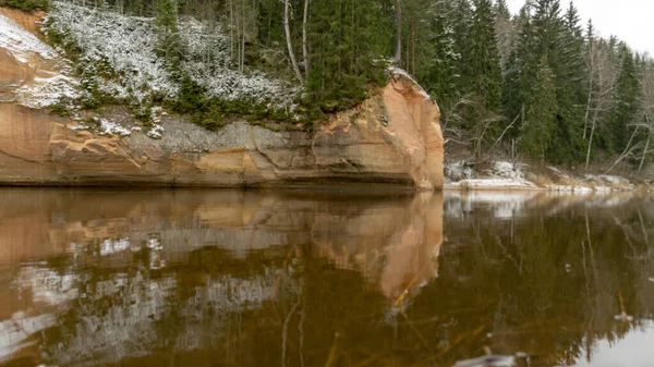 森のある川沿いの砂岩の壁 川の水の中の岩の反射 12月のゴーヤ川の景色 雪と曇りの空 ゴーヤ国立公園 エルグル崖の近くのゴーヤ ラトビア — ストック写真