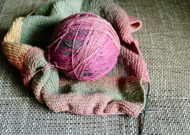 picture with variegated color balls on the knitted textile background, wool yarn and knitting tools - knitting in progress