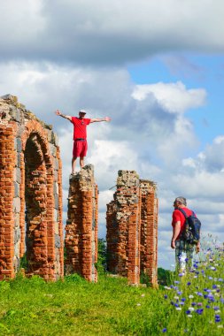 Kaya ve çiçek tarlasının ortasındaki kırmızı tuğlalardan yapılmış eski bir ahırın güzel kalıntıları harabelerin üzerindeki genç adam, yaz manzarası.