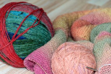 Knitted clothing, accessory in the process of creation. Knitting needles and thread ball, colorful, yellow, pink, gray fabric, woolen yarn of different colors with needles, needlework