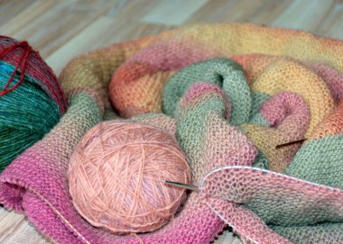 Knitted clothing, accessory in the process of creation. Knitting needles and thread ball, colorful, yellow, pink, gray fabric, woolen yarn of different colors with needles, needlework