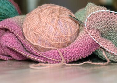 Knitted clothing, accessory in the process of creation. Knitting needles and thread ball, colorful, yellow, pink, gray fabric, woolen yarn of different colors with needles, needlework