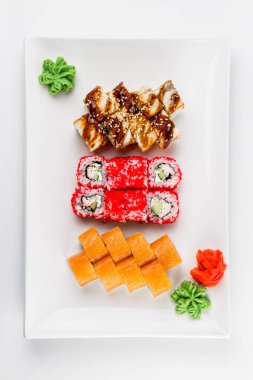 Farklı suşi ruloları, pilav, balık, salatalık, wasabi, zencefil, havyar ve susamlı. Beyaz arka planda büyük beyaz bir plaka. Bir tabakta bir sürü suşi..