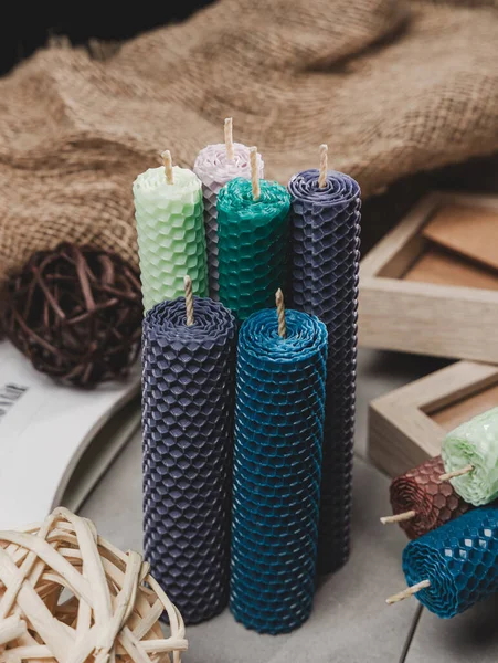 Multicolored beeswax candles with honeycomb texture on a wooden floor. Tree cuts and other accessories.
