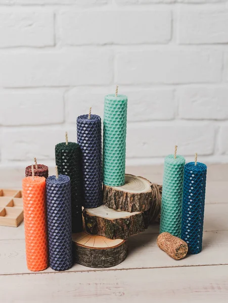 Multicolored beeswax candles with honeycomb texture on a wooden floor. Tree cuts and other accessories.