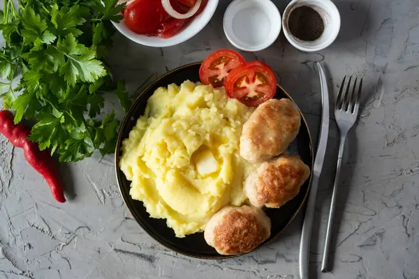 Aile için doyurucu bir akşam yemeği: patates püresi, domuz pirzolası, gri arka planda bir tabakta domates dilimleri..