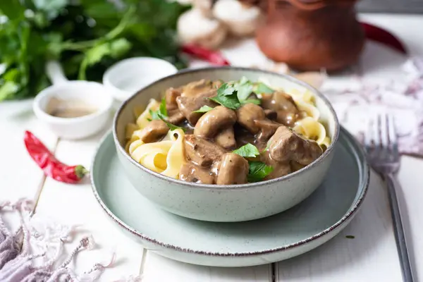 Aileye öğle yemeği için doyurucu bir yemek: mantarlı fettuccine ve beyaz bir masada güzel bir tabakta baharatlı soslu biftek. Akşam yemeği için etli ve mantarlı makarna. Yakın plan.