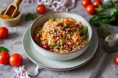 A hearty vegetarian lunch for the family: stewed buckwheat with vegetables in a beautiful plate on a gray background. Close-up
