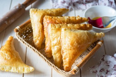 Hearty snack: Puff pastry with cheese and ham in a basket on a white table. Close-up.