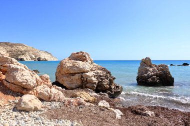 Akdeniz suyunun Afrodit Körfezi 'nde taş kayalıklı Afrodit Sahili güneşli bir arka planda mavi gökyüzü Kıbrıs' ta Petra tu Romiou